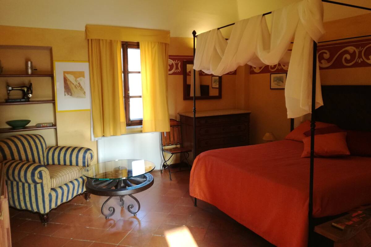 A room with a bed, a chair, a table, a dresser, and a window with curtains.