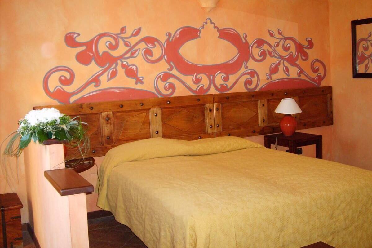 A bedroom with a wooden headboard, a bed with a yellow bedspread, a nightstand with a red lamp, and a wall decoration.