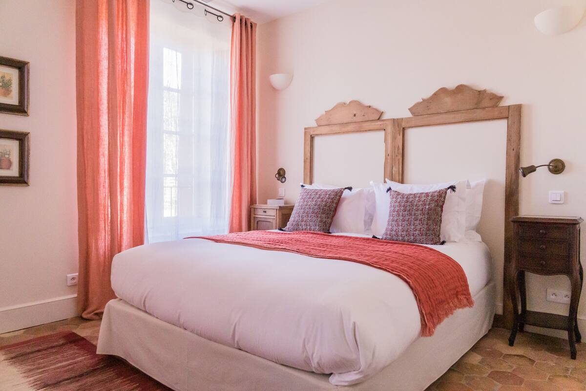 Un dormitorio con una cama grande, cabecera de madera, una mesita de noche y una manta roja.