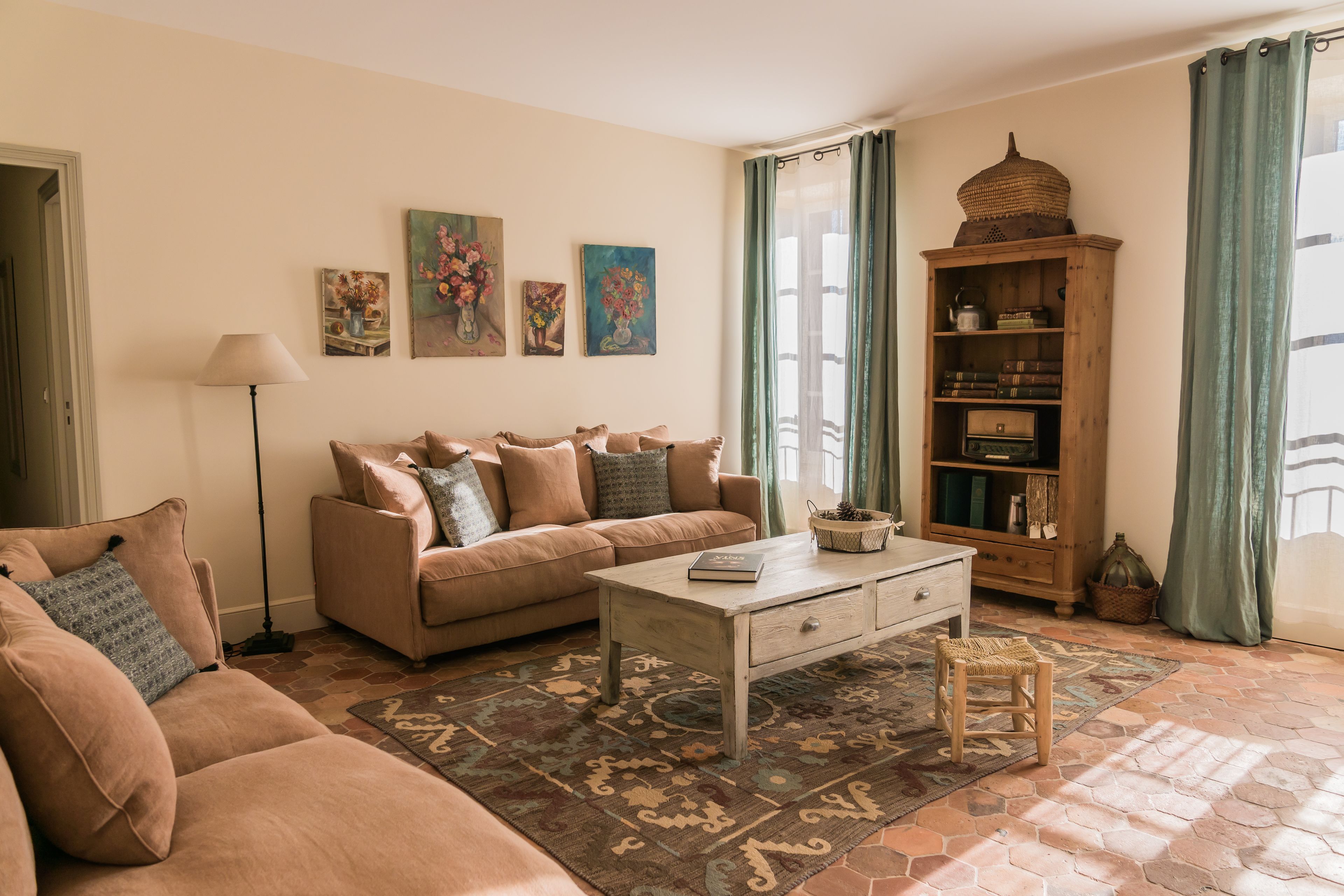 Un salón con un sofá beige, una mesa de centro y un tapete estampado. Hay cuadros en la pared y un aparador de madera con libros y adornos.
