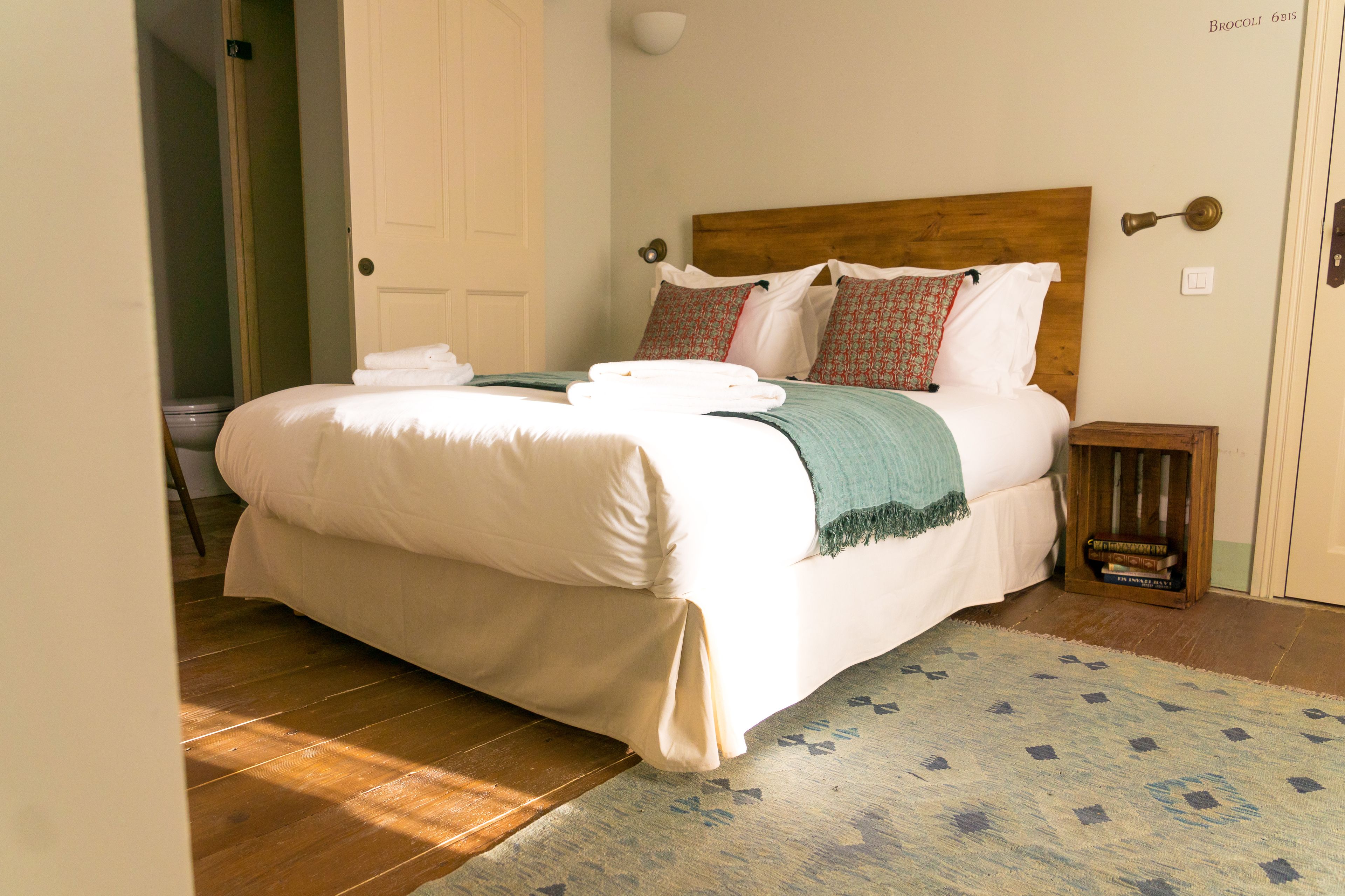 A neatly made bed with white linens, a wooden headboard, and a small bedside table with a book.