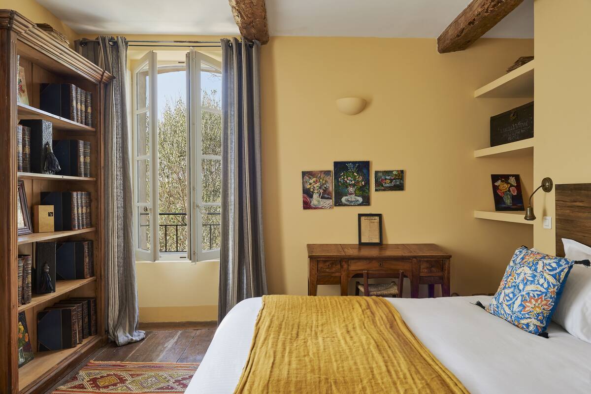 Una habitación con una cama, un escritorio de madera, una estantería y una ventana con cortinas.