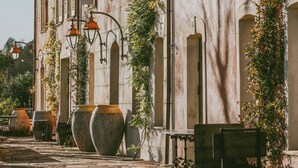Un bâtiment historique doté de fenêtres en arc de cercle et de volets, d’un espace extérieur aménagé pour s’asseoir et de grands jardinières.