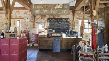 A rustic interior with wooden beams, stone walls, and a sign reading "Fromages Fermiers."