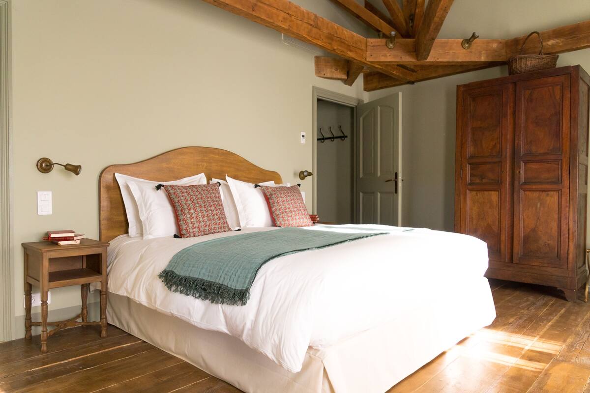 Un dormitorio con una cama de madera, una mesita de noche, un armario de madera y una puerta con perchero.