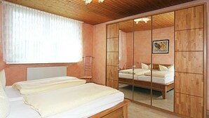A bedroom with a wooden bed, a large mirror, and a window with curtains. - Vacation home Nicole - Holiday homes Friesensterne (Esens)