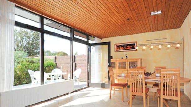 A dining area with a wooden ceiling, large windows, and a view of greenery outside. - Vacation home Nicole - Holiday homes Friesensterne (Esens)