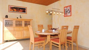 A dining area with a round table, six wooden chairs with red cushions, a wooden cabinet with glass doors, and two framed pictures on the wall. - Vacation home Nicole - Holiday homes Friesensterne (Esens)