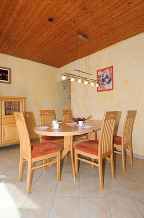 A dining area with a wooden table and chairs, a ceiling light fixture, and a framed picture on the wall.