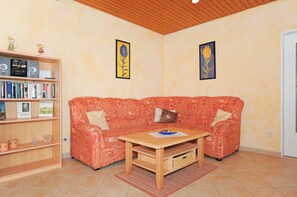 A living room with a red patterned sofa, a wooden coffee table, a bookshelf, and two framed pictures on the wall.
