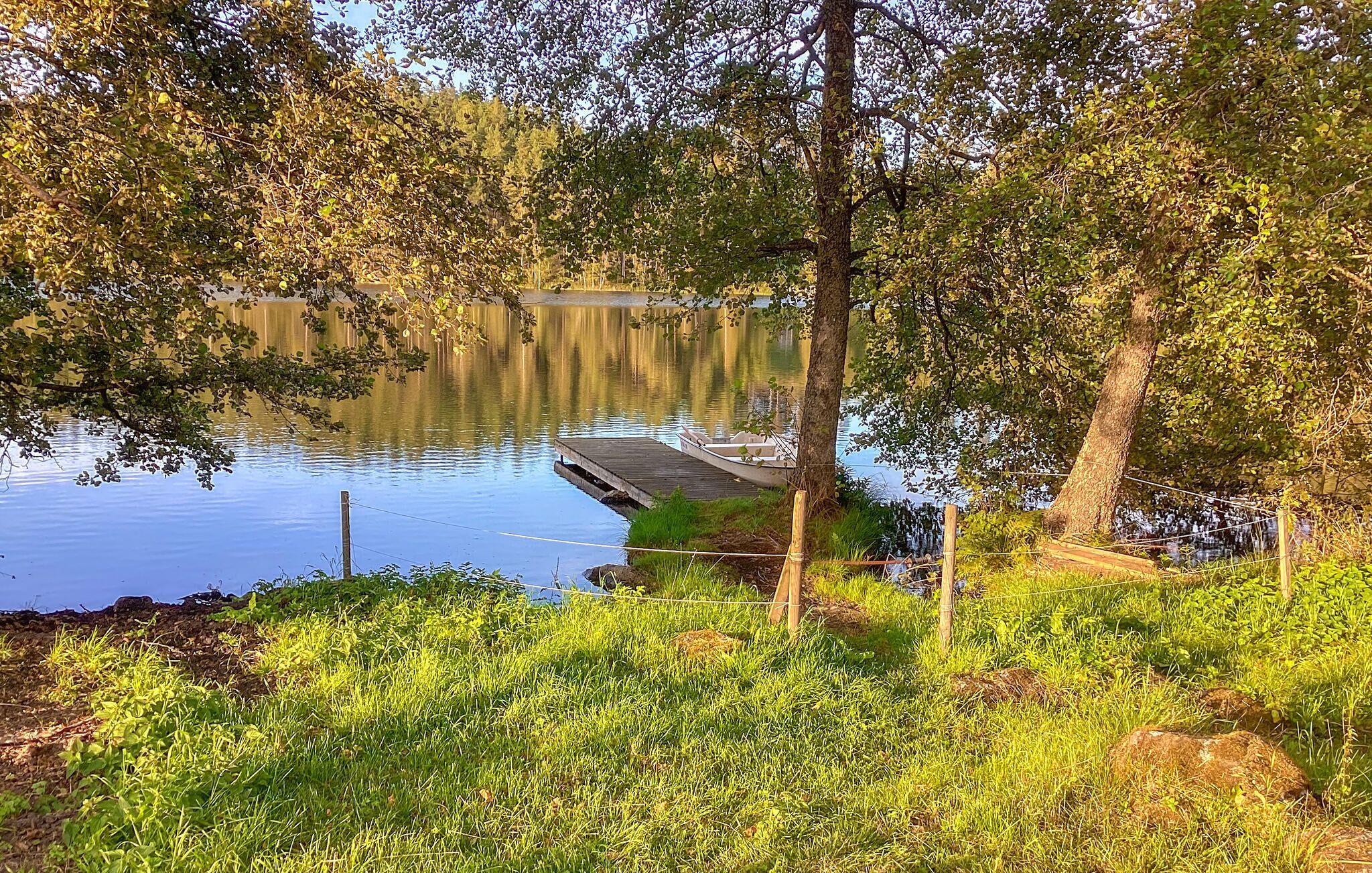 A serene lakeside scene with a dock extending into calm water, surrounded by lush greenery and trees.