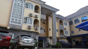 Un edificio residencial de varios pisos con balcones, unidades de aire acondicionado y un área exterior techada con asientos.