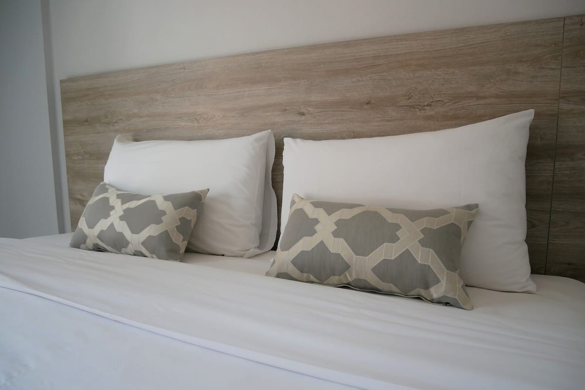 A bed with a wooden headboard, two white pillows, and two patterned pillows.