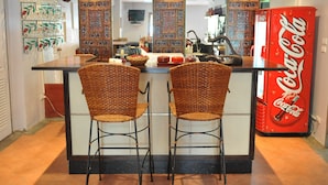 A kitchen with a central island, two wicker chairs, a Coca-Cola refrigerator, and decorative wall panels. - Drop Inn Bangkok (Bangkok)
