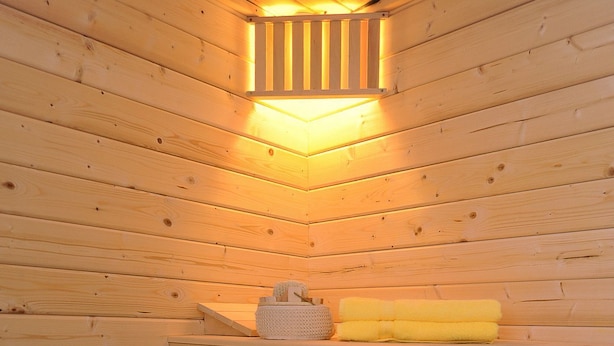 A wooden sauna with a bench, a bucket with a ladle, and a shelf with towels and a container. - Holiday house Nordseewoge - Holiday homes North Sea Trio (Esens)