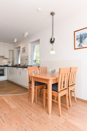 Une cuisine moderne avec des meubles blancs, une table à manger en bois et un luminaire suspendu.