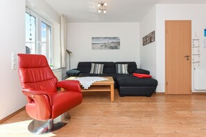 Un salon avec un fauteuil rouge, un canapé noir, une table basse en bois et un tableau accroché au mur.