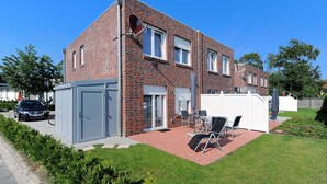 A two-story brick house with a patio area featuring a table and chairs, a car parked outside, and a small shed. - Holiday house Nordseewoge - Holiday homes North Sea Trio (Esens)
