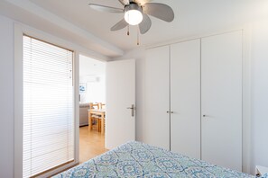 A bedroom with a bed, a ceiling fan, a wardrobe, and a door leading to a dining area. - Modern Holiday Apartment "Arena" With Sea View (Conil de la Frontera)