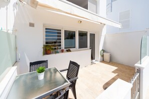 A patio with a table and chairs, a potted plant, and a window with blinds. - Modern Holiday Apartment "Arena" With Sea View (Conil de la Frontera)