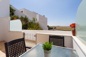 A balcony with a table and chairs, a potted plant, and a view of the countryside. - Modern Holiday Apartment "Arena" With Sea View (Conil de la Frontera)