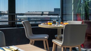 A dining area with a table set for two, a window with a view of buildings, and a potted plant. - Appart’hôtel Odalys City - Nantes Cité des congrès (Nantes)