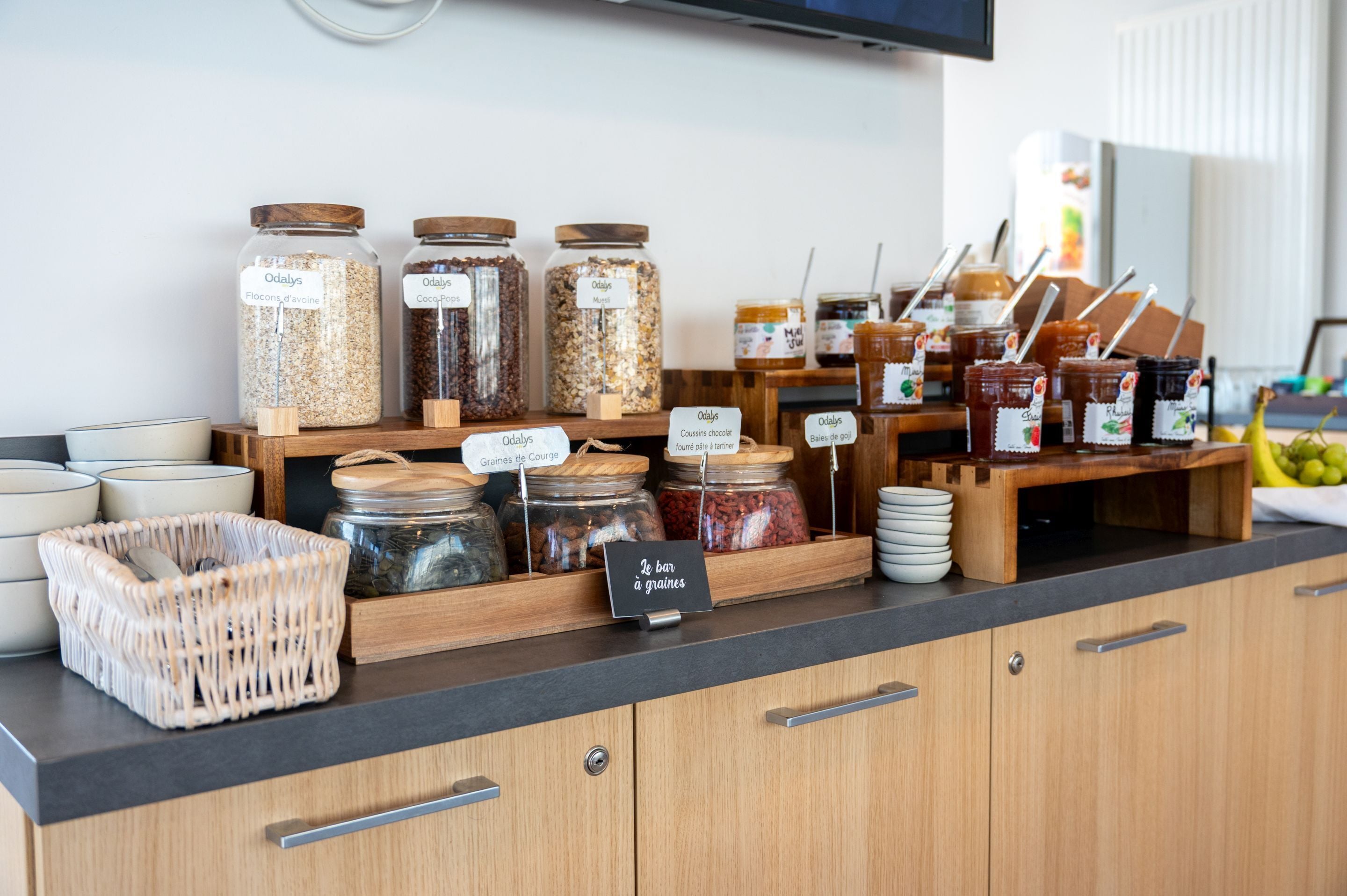 A kitchen counter with various jars of grains and spreads, a wicker basket, and a sign indicating a grain bar.