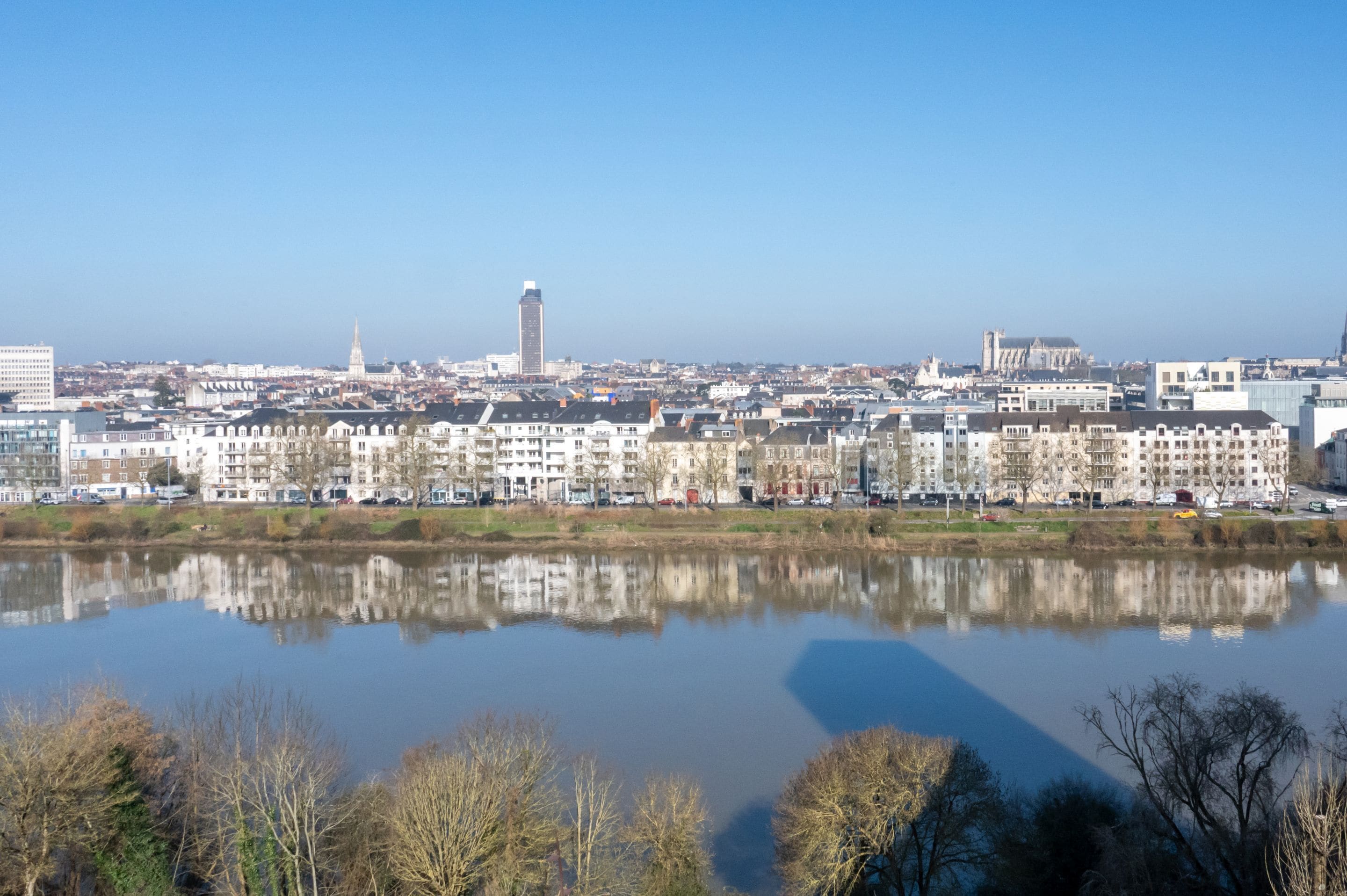 A cityscape with buildings along a river, a clear sky, and reflections in the water.