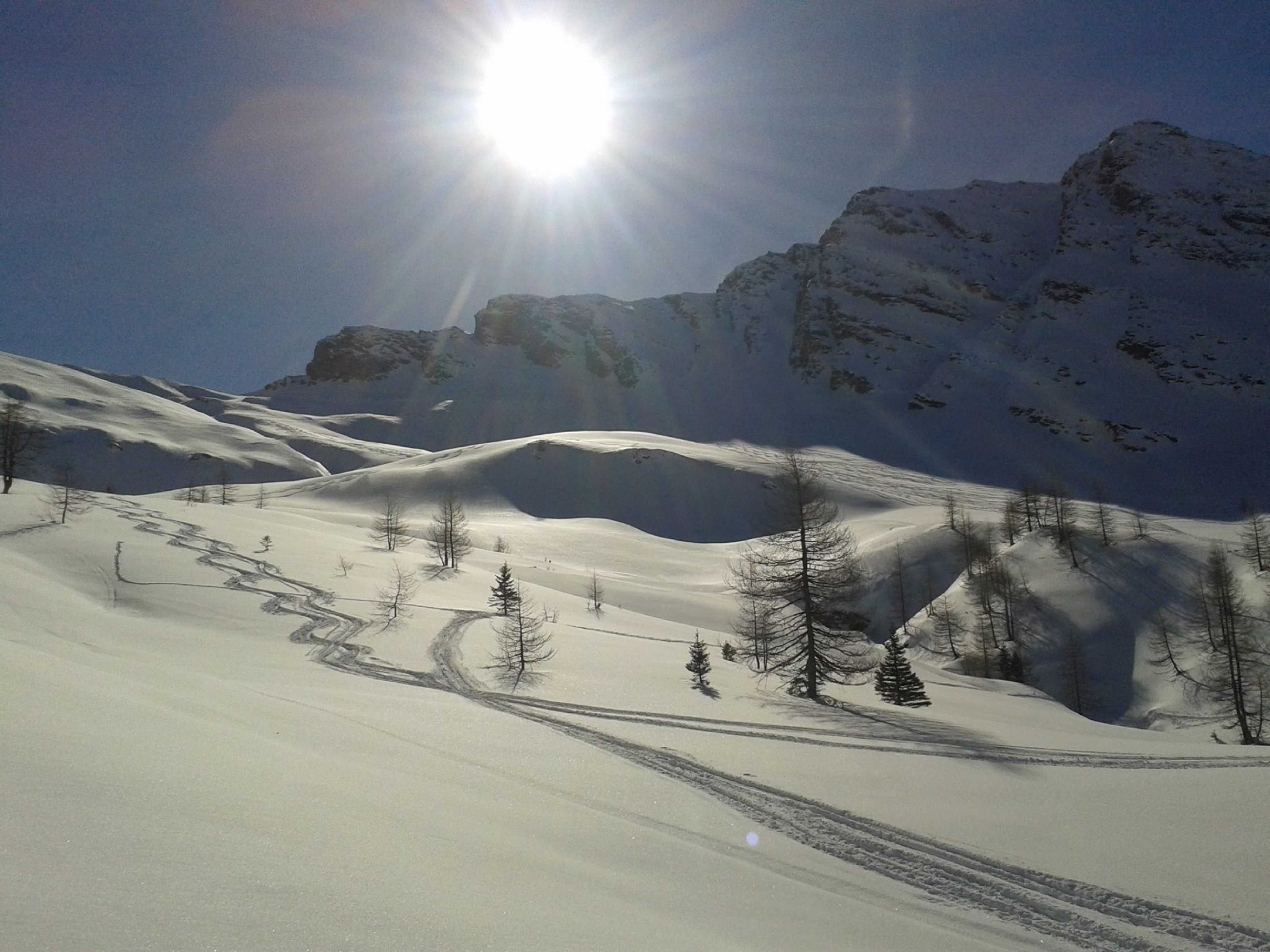 Paesaggio montuoso innevato con cielo sereno e il sole splendente.