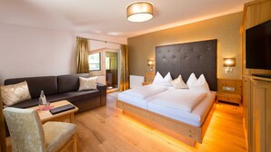 A hotel room with a bed, a sofa, a TV, a bedside table, and a window.