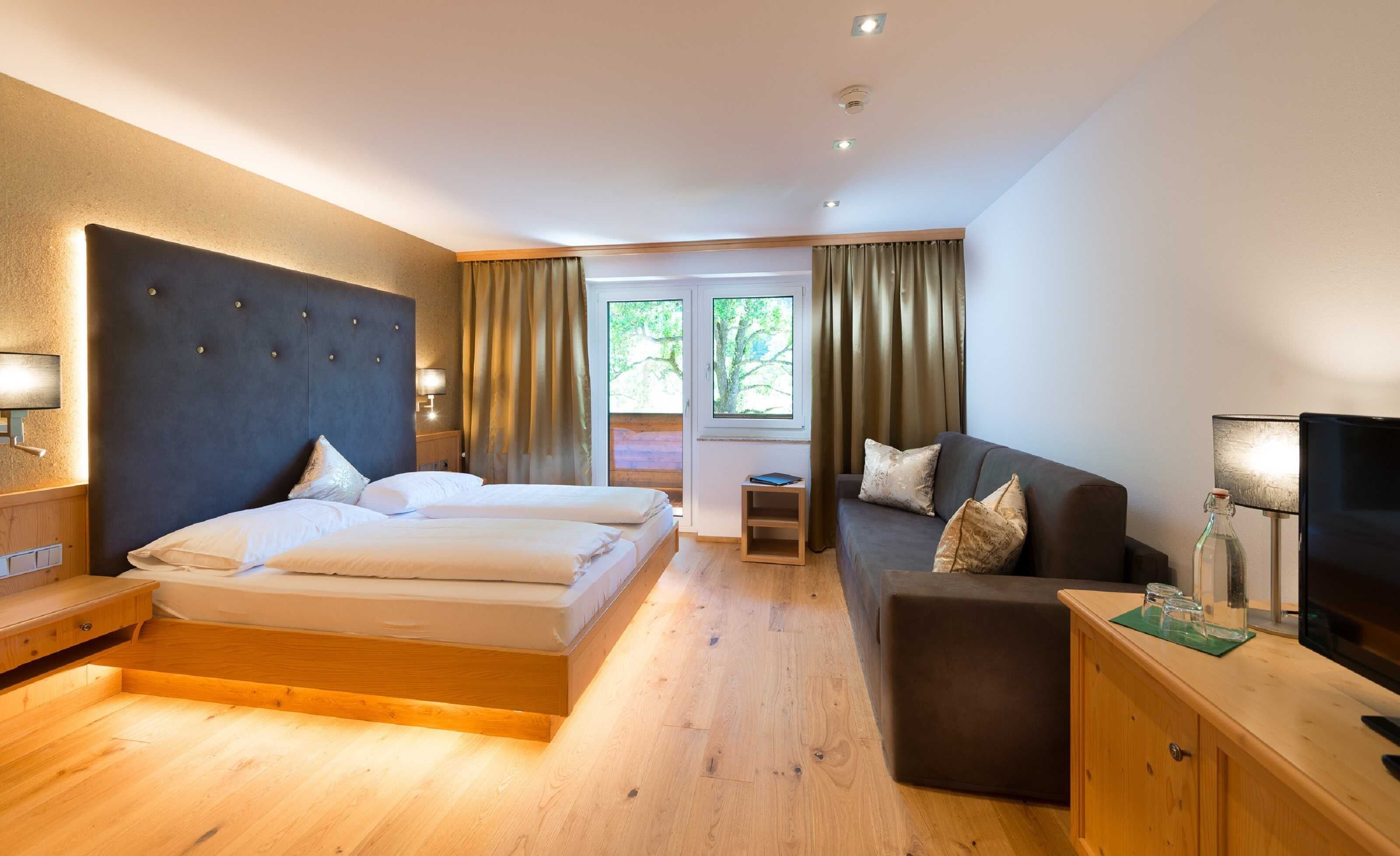 Habitación de hotel con cama, sofá, televisión y ventana con cortinas.