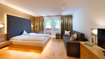 Habitación de hotel con cama, sofá, televisión y ventana con cortinas.
