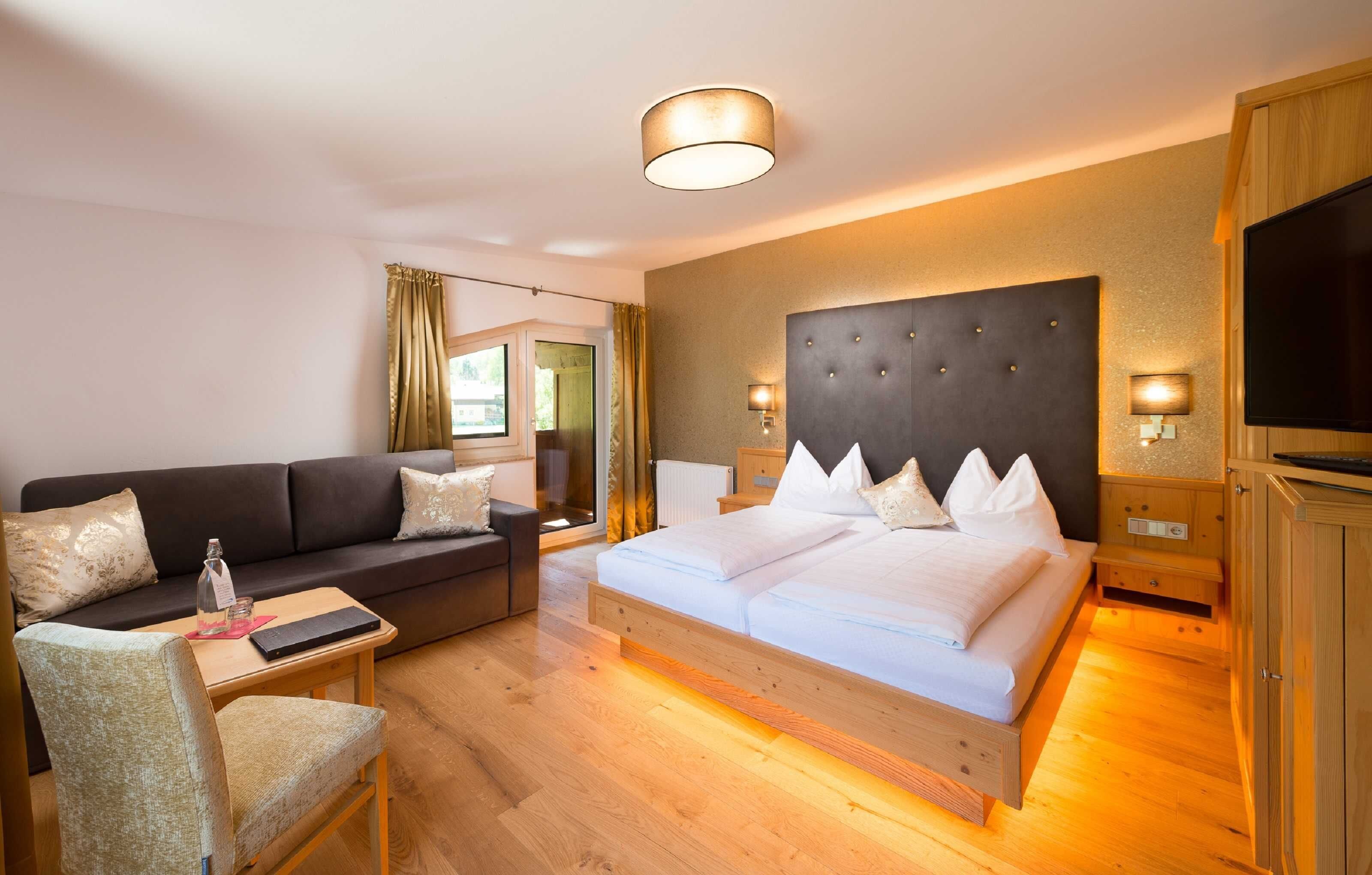 Una camera d'albergo con un letto, un divano, una TV, un comodino e una finestra.