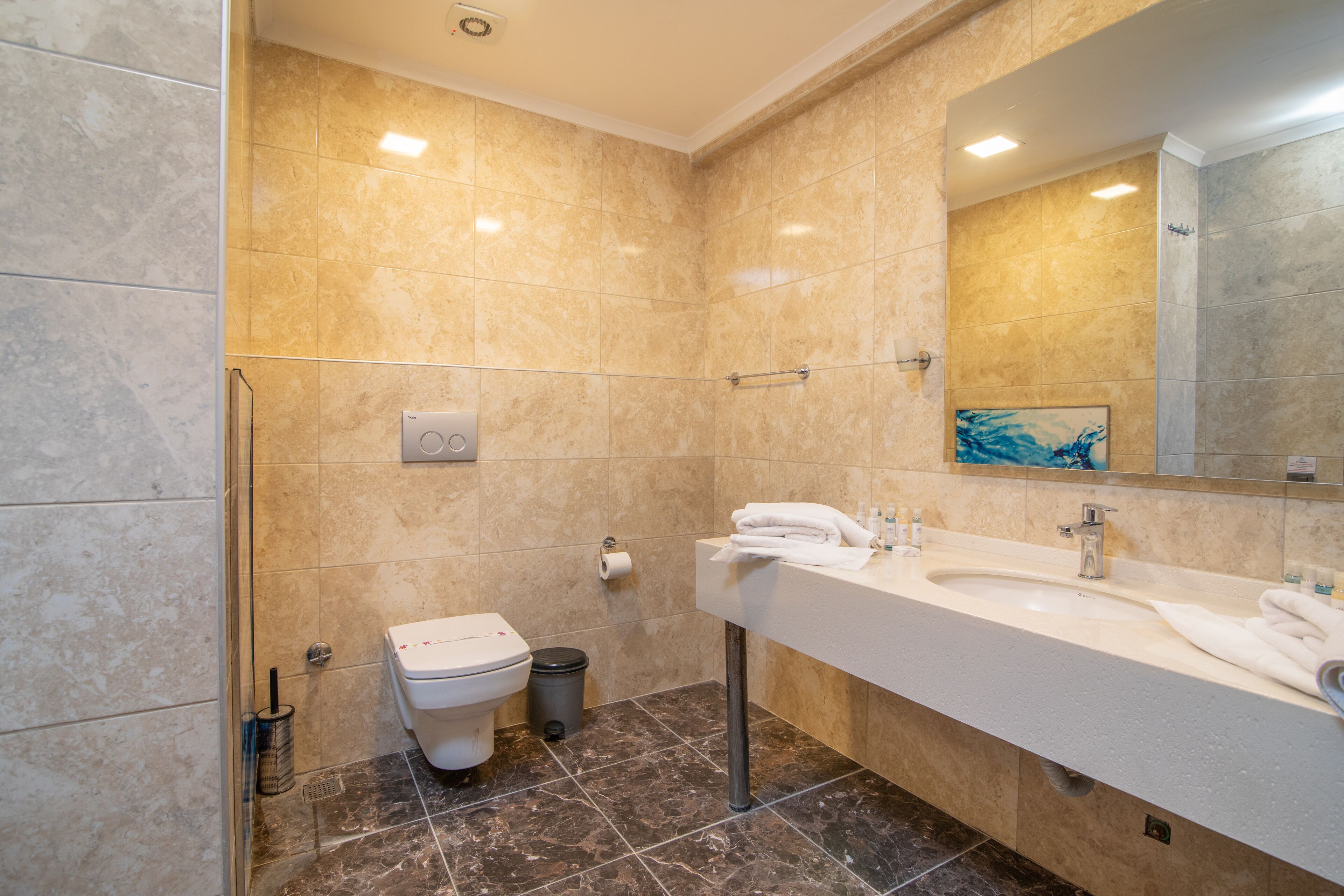 A modern bathroom with a marble floor, a white sink, a mirror, and a toilet.