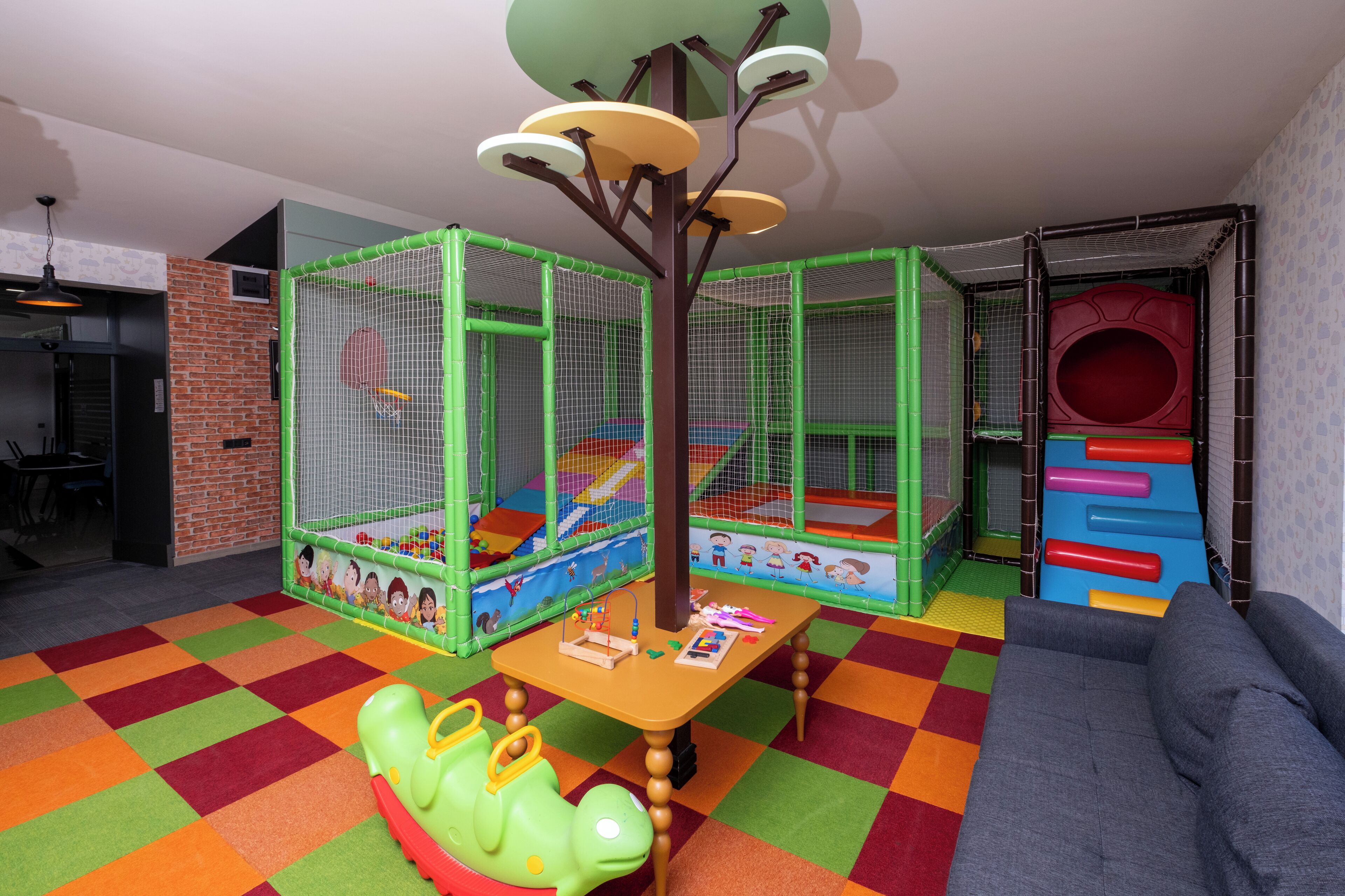 Un área de juegos con una mesa de juegos suaves, un corralito verde y un tobogán.