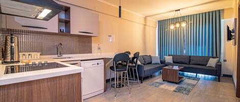 Una cocina moderna con lavavajillas, un comedor con sofá y sillas, y una sala de estar con un gran ventanal y cortinas.