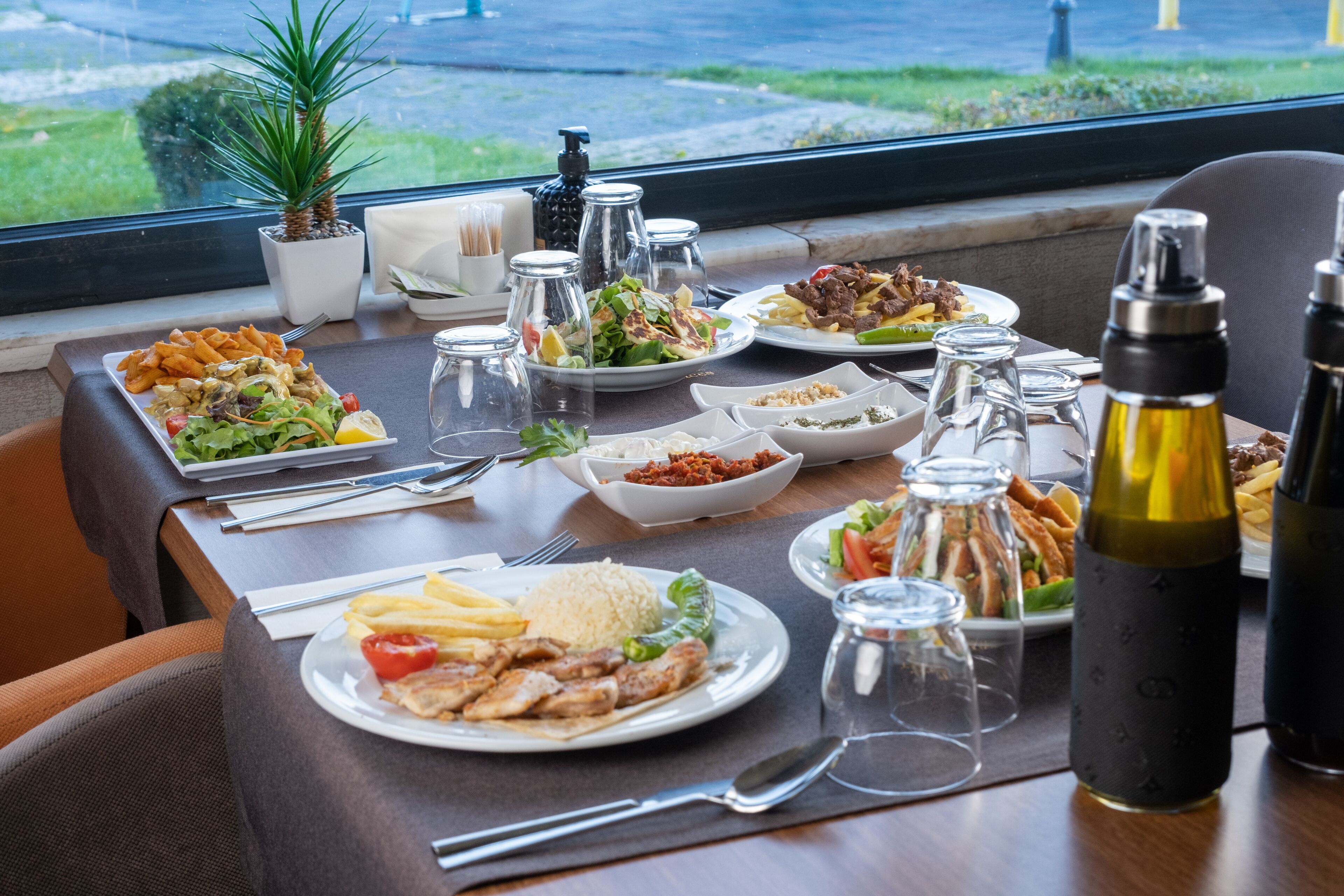A dining table set with various dishes, including salads, meats, and rice, with salt and pepper shakers, and a potted plant.