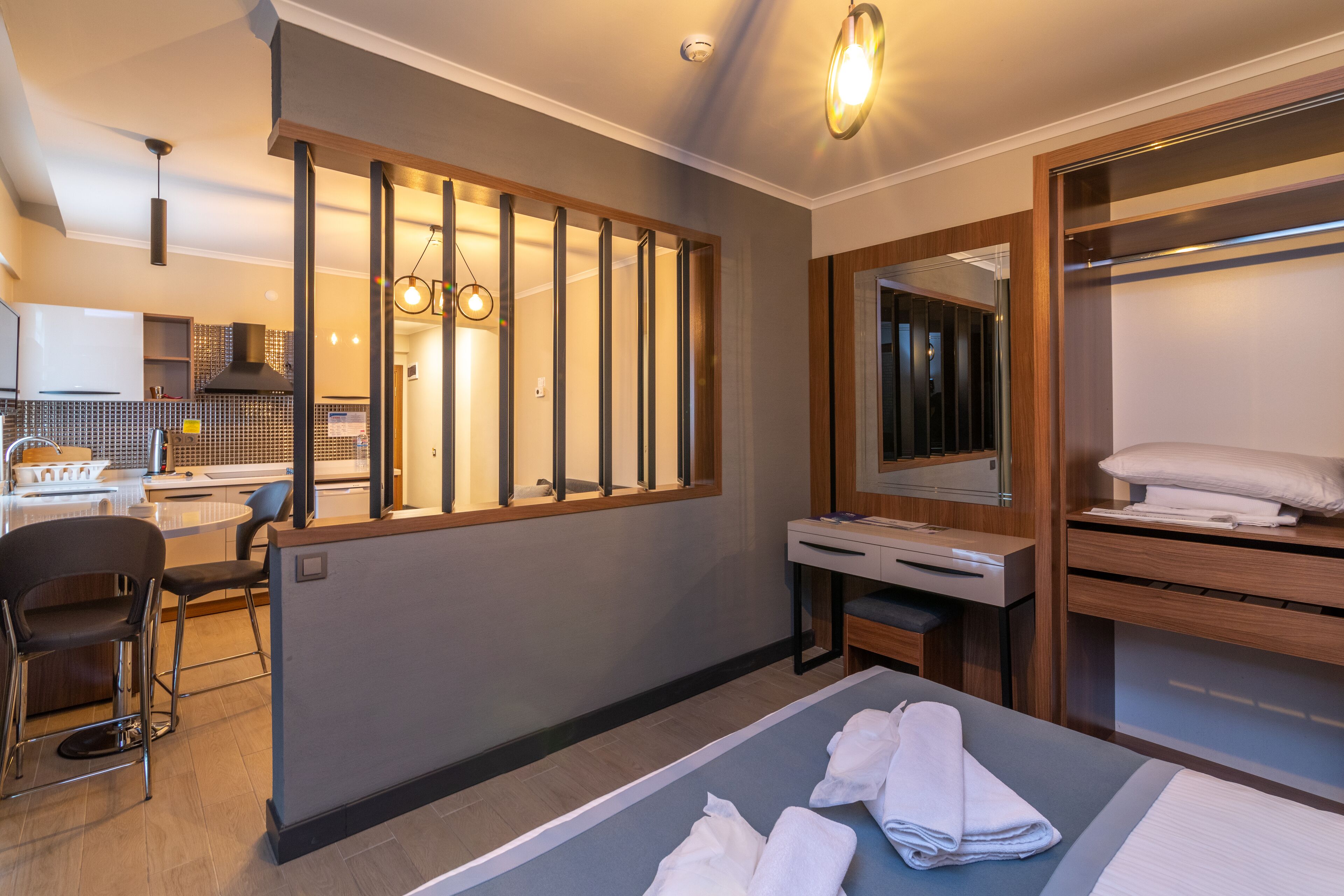 A modern hotel room with a bed, a desk, a chair, and a bathroom with a mirror and towel rack.