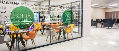 Interior moderno de una cafetería con paredes de vidrio, diversas opciones de asientos y un llamativo letrero de 'FORIA CAFE'.