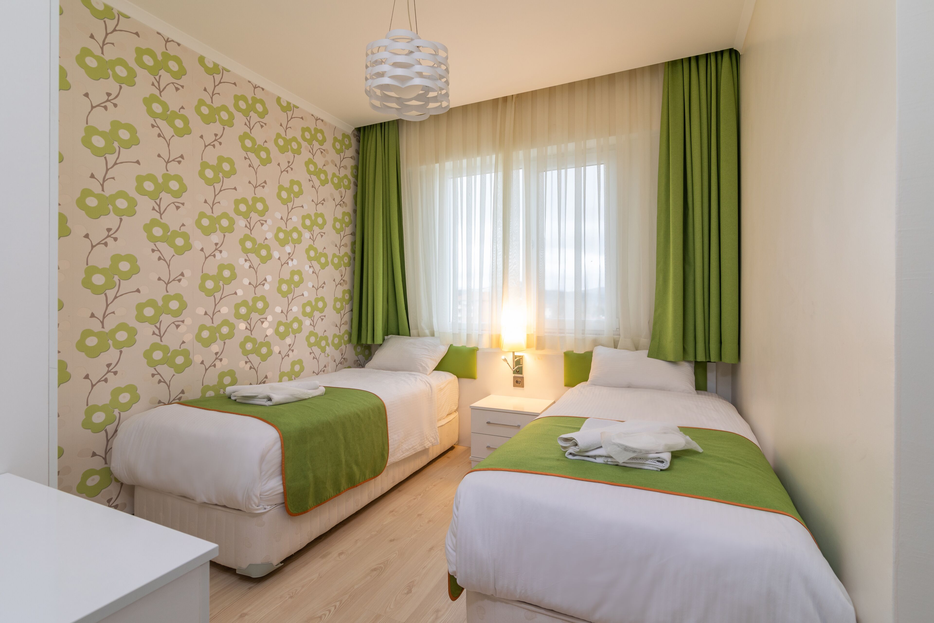 Une chambre d’hôtel avec deux lits, une table de chevet, une commode et une fenêtre avec des rideaux.