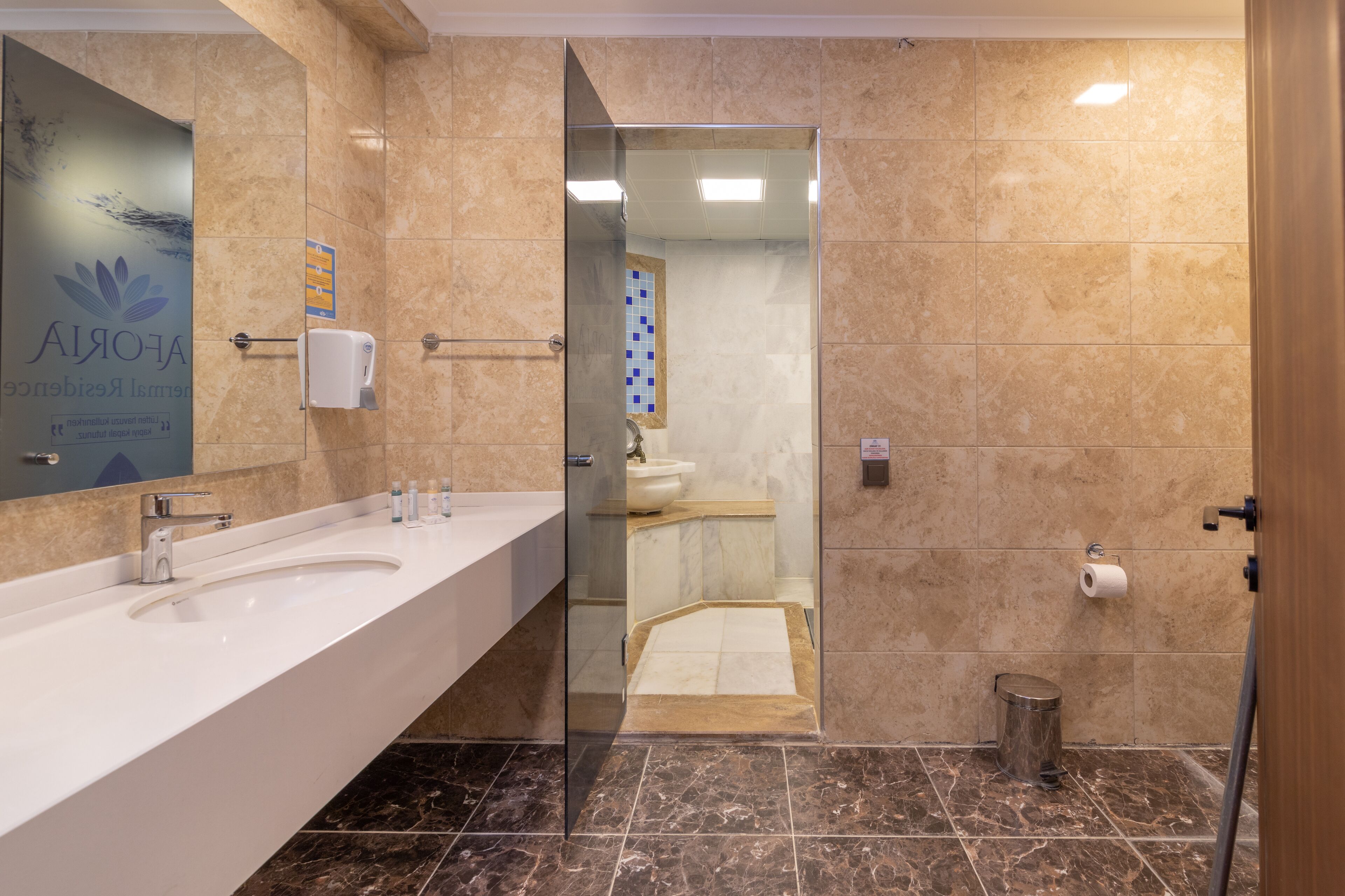 A modern bathroom with a large sink, a glass shower enclosure, and a marble-tiled floor.