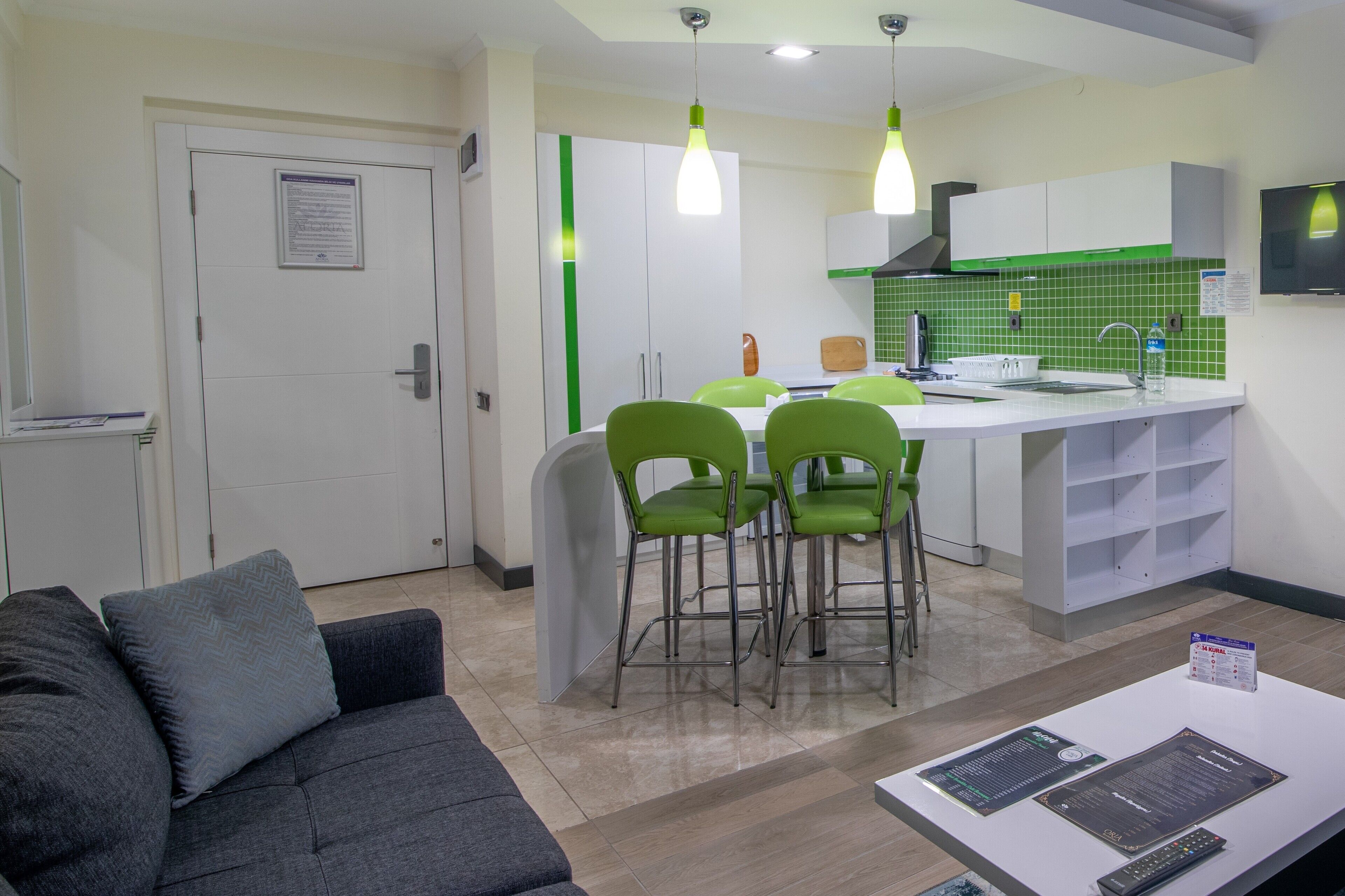 Una cocina moderna con detalles verdes, un comedor con sillas verdes y una sala de estar con un sofá gris.