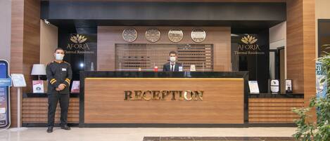 Un comptoir d’accueil avec un revêtement en bois, une plaque nominative indiquant « RÉCEPTION » et quatre horloges placées au-dessus.
