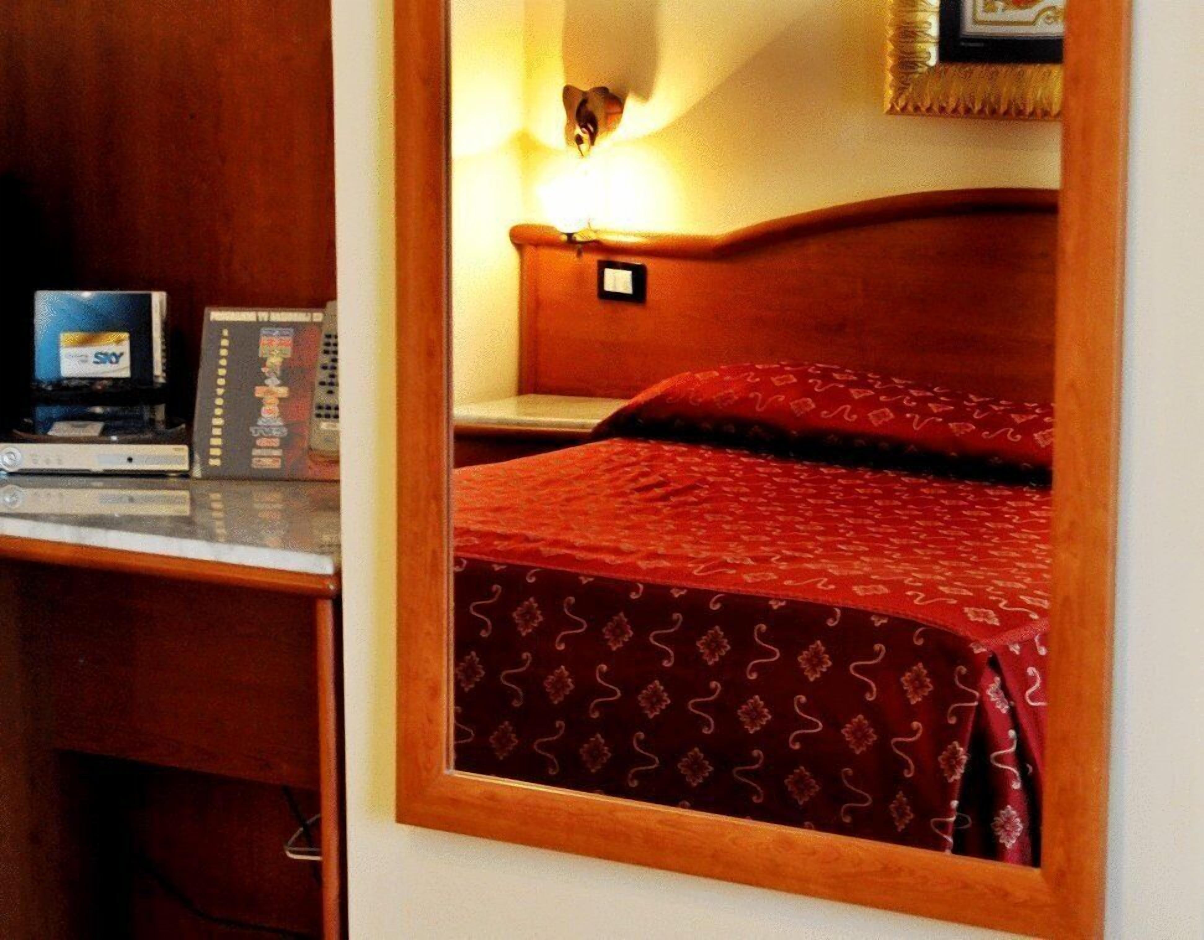 A hotel room with a bed, a desk with a computer, and a lamp.