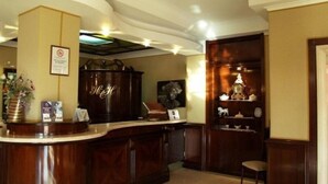 A reception desk with a wooden finish, a framed sign above it, and a chair to the right. - Hermitage Capua Hotel (Vitulazio)