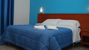 Una cama con edredón azul, almohadas blancas y dos toallas blancas dobladas.