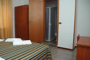 Habitación de hotel con cama, armario de madera, zona de ducha y un pequeño escritorio de madera.