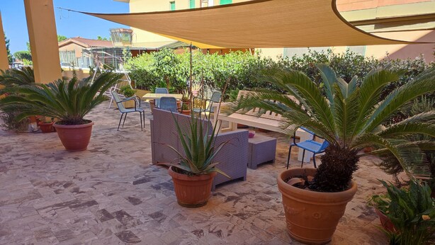 Un patio al aire libre con plantas en macetas, mobiliario de mimbre y suelo de baldosas.