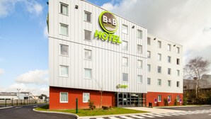 A modern B&B hotel with a prominent logo, a flat facade, and a well-maintained lawn.