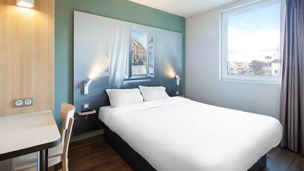 A hotel room with a large bed, a desk, and a window with curtains.